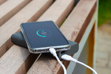 Smartphone connected to a portable power bank showing battery charging progress on the screen. Modern mobile technology concept with charging cable and digital battery indicator.