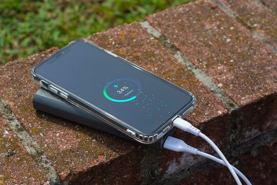 Smartphone connected to a portable power bank showing battery charging progress on the screen. Modern mobile technology concept with charging cable and digital battery indicator. - Powered by Adobe