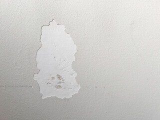 A patch of peeling paint exposes rough underlying layers on a light-colored wall. 