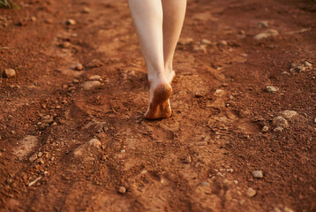 Close up of female bare feet walking on soft red clay ground. Concept of earthing and connecting with nature, with ample copy space.