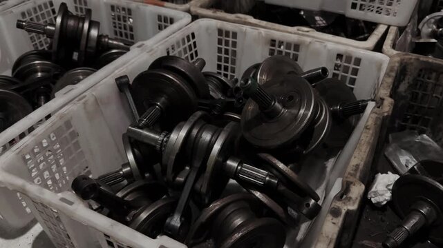 A collection of engine crankshafts and connecting rods stored in plastic crates within a workshop. Motorcycle Machine Part