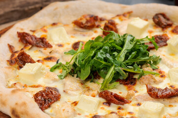 pizza with cheese and sun-dried tomatoes and fresh arugula on a wooden board, macro photo