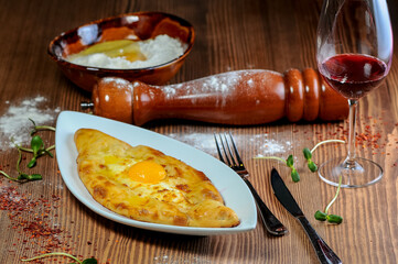 Khachapuri with cheese and egg yolk in a white plate on a table with wine