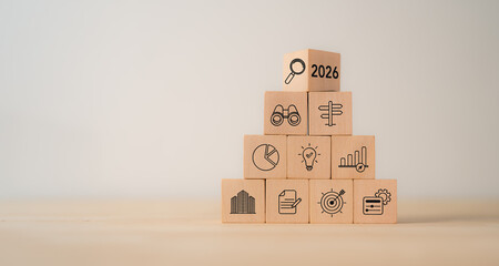 Obraz premium Economic, business outlook concept. Financial, business view or economic growth forecast for 2026. OUTLOOK 2026 text and business trend icons on wooden cube blocks, copy space, minimal background.