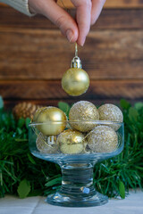 Hand holding gold glitter bauble above festive bowl.