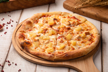 Classic Hawaiian pizza topped with pineapple, cheese and ham served on a wooden board on rustic table
