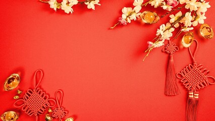 Vibrant red background with traditional Chinese New Year decorations including gold ingots, decorative knots, and delicate blossoms, symbolizing prosperity and good fortune.