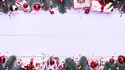 Festive Christmas border with fir branches, ornaments, candy canes, and gifts on a white wooden background, perfect for holiday greetings and celebrations.