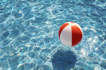 A red and white beach ball floating in the water of an outdoor swimming pool on a sunny summer day