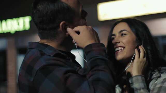 Loving couple sharing headphones and laughing while listening to music at night
