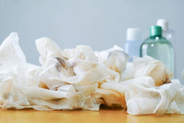 Pile of used cleansing wipes in foreground with blurred skincare bottles behind. Represents everyday woman rituals, realistic beauty care, and amount of disposable waste in the cosmetics industry.