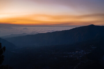 Golden hour lights up a mountain range with clouds creating a blanket of mist in the distance