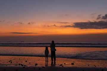 Naklejka premium Silhouettes on the beach: Mother and child enjoying a vibrant sunset over the ocean's horizon