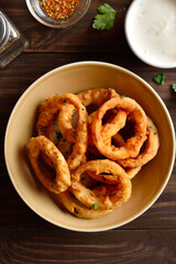 Crispy fried onion rings in bowl on wooden table