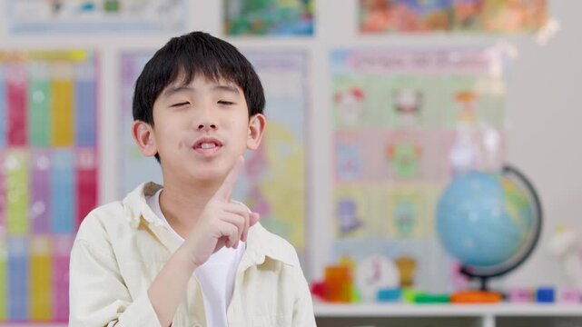 Asian schoolboy gesturing quiet sign in colorful classroom