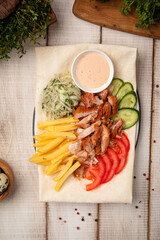 Doner plate with sliced chicken fries fresh vegetables and sauce served on lavash in rustic restaurant style
