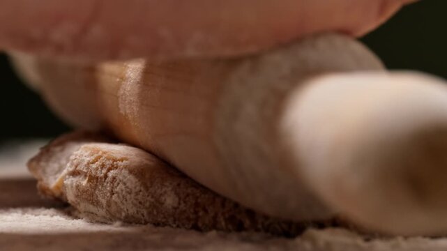 Side view close-up of female hands using a rolling pin to flatten dough on a floured surface. Homemade baking process captured in soft light, symbolizing warmth and tradition.