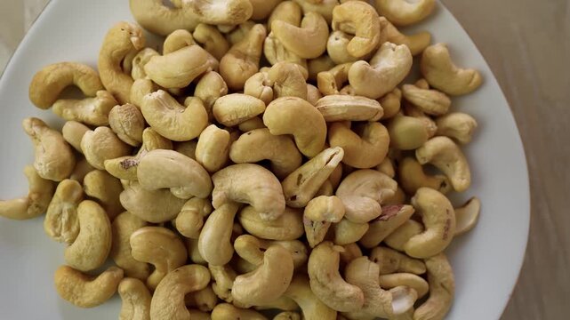 Plate filled with raw cashew nuts on a wooden table