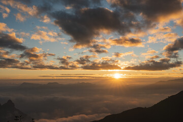 Golden hour illuminates the mountain peaks with clouds dancing around the sun's glow
