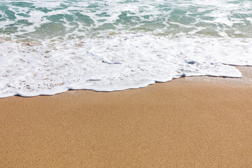 Sunlit beach shore with gentle waves lapping onto golden sand