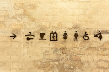 Set of facility icons on a brick wall indicating restroom, accessibility, and elevation signs