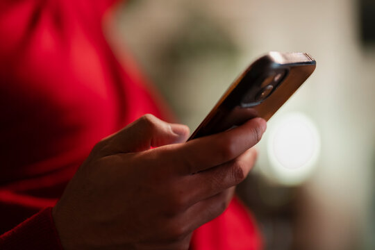 A person's hand holds a smartphone, fingers interacting with the screen. The background is a soft blur of red and neutral tones.