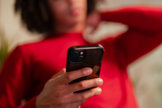 A person in a red top holds a smartphone, touching their neck with their other hand.