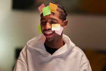 A young man with colorful sticky notes on his face laughs heartily, conveying a sense of playful chaos and creative brainstorming.
