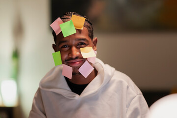 A young man with colorful sticky notes on his face smiles, representing ideas, tasks, or reminders.