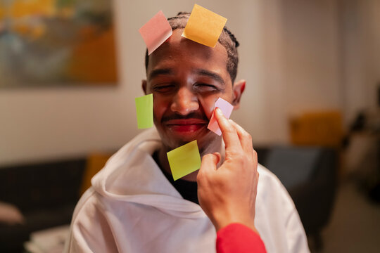 A person places colorful sticky notes on another person's face, creating a playful and creative moment.