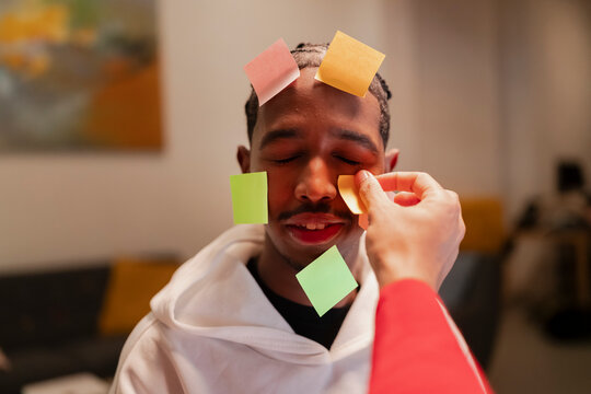 A person places colorful sticky notes on another person's face, creating a playful and creative moment.