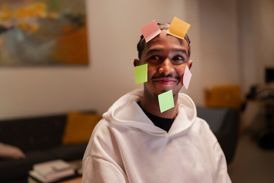 A young man with colorful sticky notes on his face smiles playfully, suggesting a moment of lightheartedness or a creative brainstorming session.