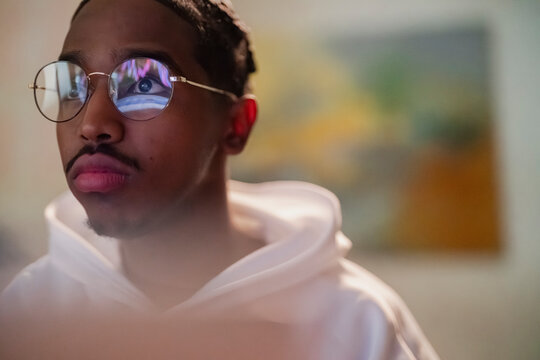 A young man wearing round glasses looks intently at a screen, his eye reflecting a colorful graph.