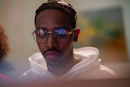 A young man wearing glasses looks intently at a screen displaying a financial chart, reflecting the data in his lenses.