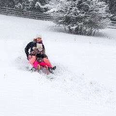 Mother and child sledding downhill on snowy hillside during calm winter family moment