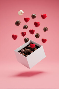 Valentine's Day Box of Chocolates with Red and Dark Heart Candies Exploding Upwards from a White Floating Container on Pink Copy Space