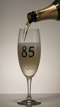 Glass engraved with the number 85. Champagne bottle fills the glass with alcohol. Celebrating milestone, anniversary or birthday