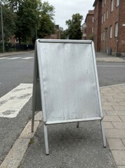 Blank A frame sidewalk sign on urban street outside storefront.