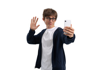 Casual man in glasses wearing white t-shirt and hoodie waving while taking a selfie with smartphone, isolated on white background, concept of communication