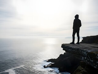 Silhouette of a person standing on a cliff edge overlooking the ocean