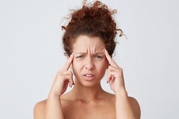 Horizontal shot of stressed depressed yong woman with curly hair and perfect skin touching temples and feels stressed after hard day isolated over white background Suffered from headache