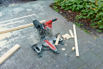 battery powered miter saw lies outside on the street with wood debris around it