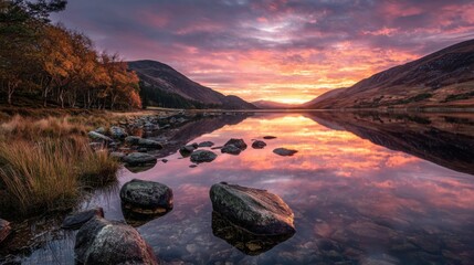 Sunset over a lake with mountains and trees near a rocky shore in a valley during the evening hours
