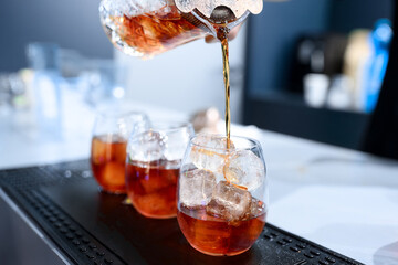 A bartender pours a vibrant pink cocktail through a fine mesh strainer into a stemless wine glass filled with ice