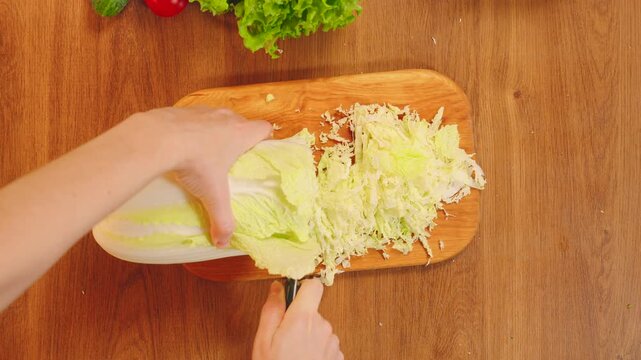 Close up shot person hands with knife cutting Chinese naba cabbage on wooden board top view. healthy food vegetable diet dinner. woman preparing vegan fresh green salad on table white kitchen home