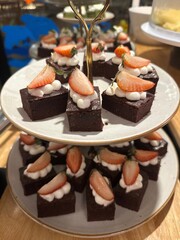 vertical photo of mini strawberry brownies with cream and berry slices arranged on a tiered stand
