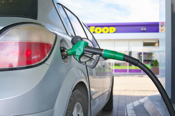 Refueling gun inserted into silver car s fuel tank with diesel or petrol.