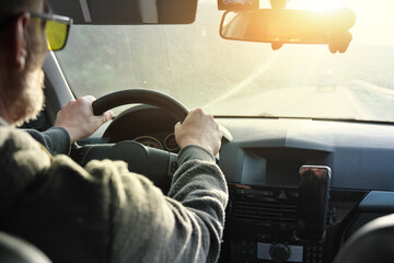 Men&rsquo;s driver's hand holding steering wheel of car while driving.