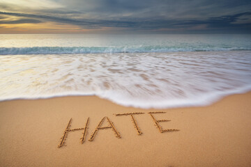 Hate word written on the sea shore during sunset.