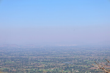 Mhaismal, MH, India, Dec 12: Expansive, distant view of a large, hazy agricultural valley and scattered small towns, stretching to the horizon under a pale, washed-out sky.